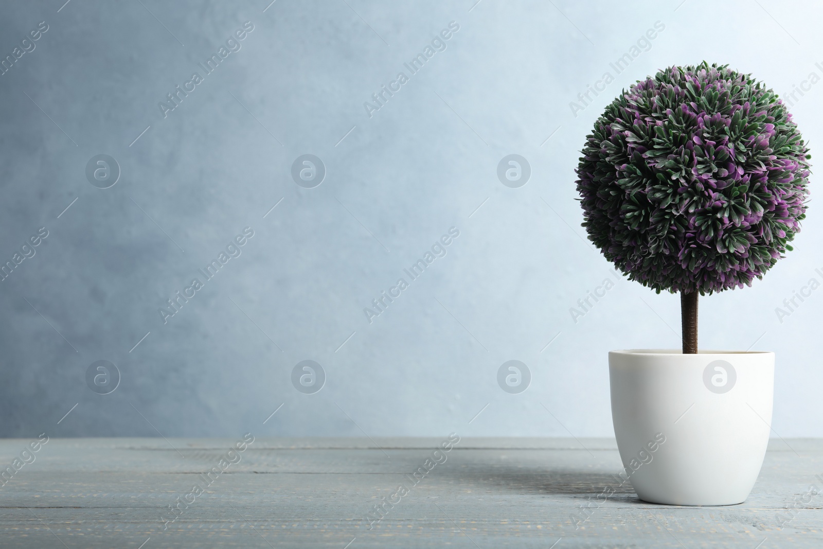 Photo of Artificial plant in flower pot on light grey wooden table. Space for text