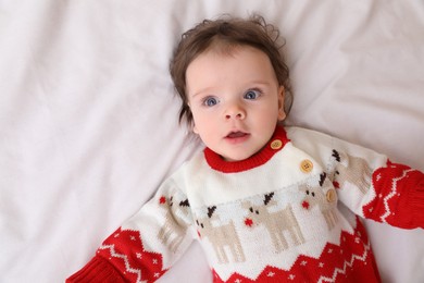 Photo of Cute little baby in Christmas sweater on soft bed, top view. Space for text
