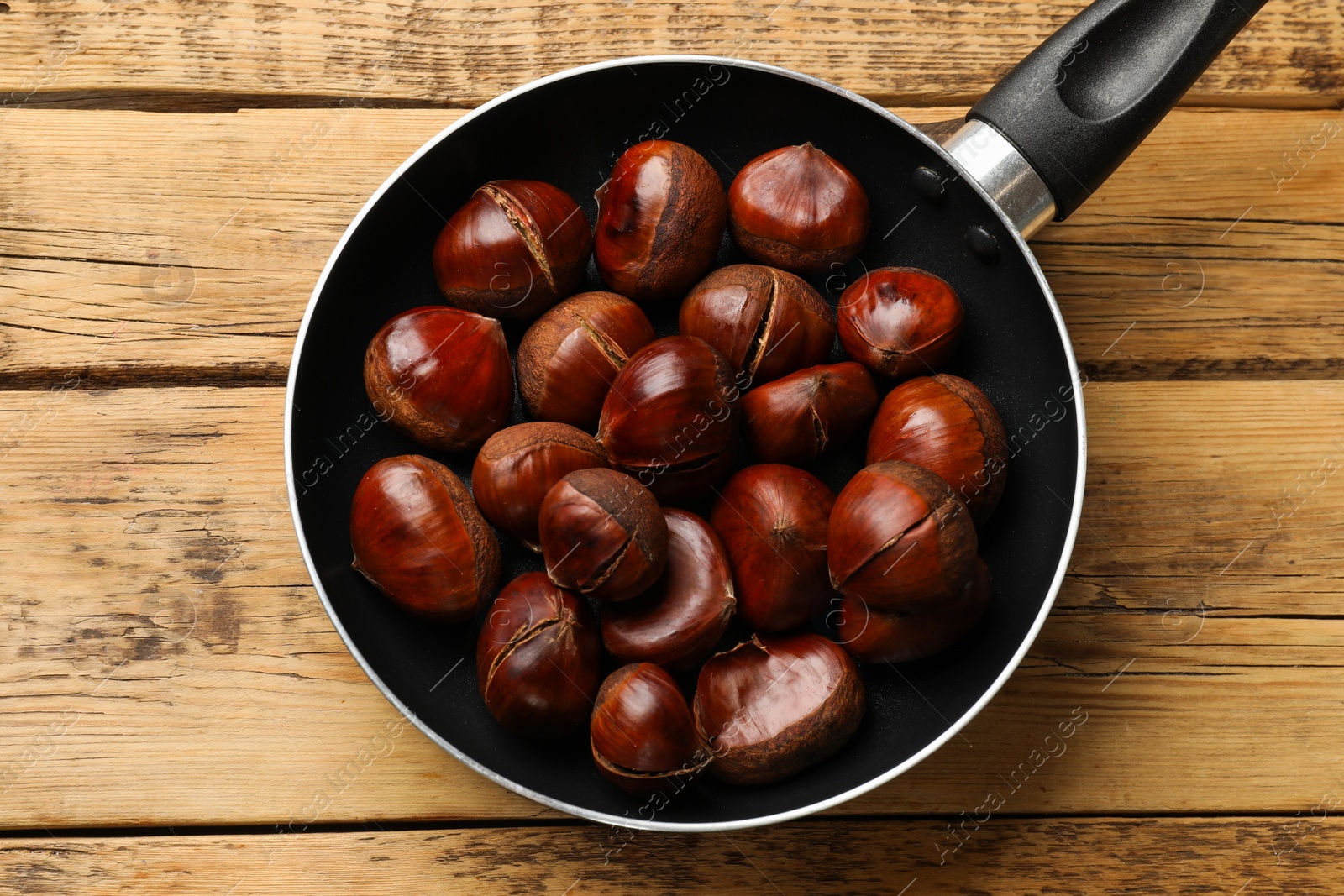 Photo of Fresh edible sweet chestnuts in frying pan on wooden table, top view