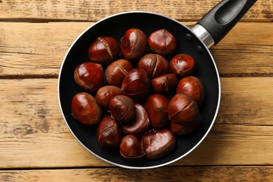 Photo of Fresh edible sweet chestnuts in frying pan on wooden table, top view
