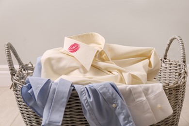 Photo of Men's shirt with lipstick kiss marks among other clothes in laundry basket indoors, closeup