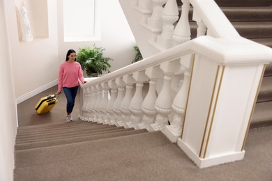 Photo of Beautiful young woman with suitcase going up stairs in hotel