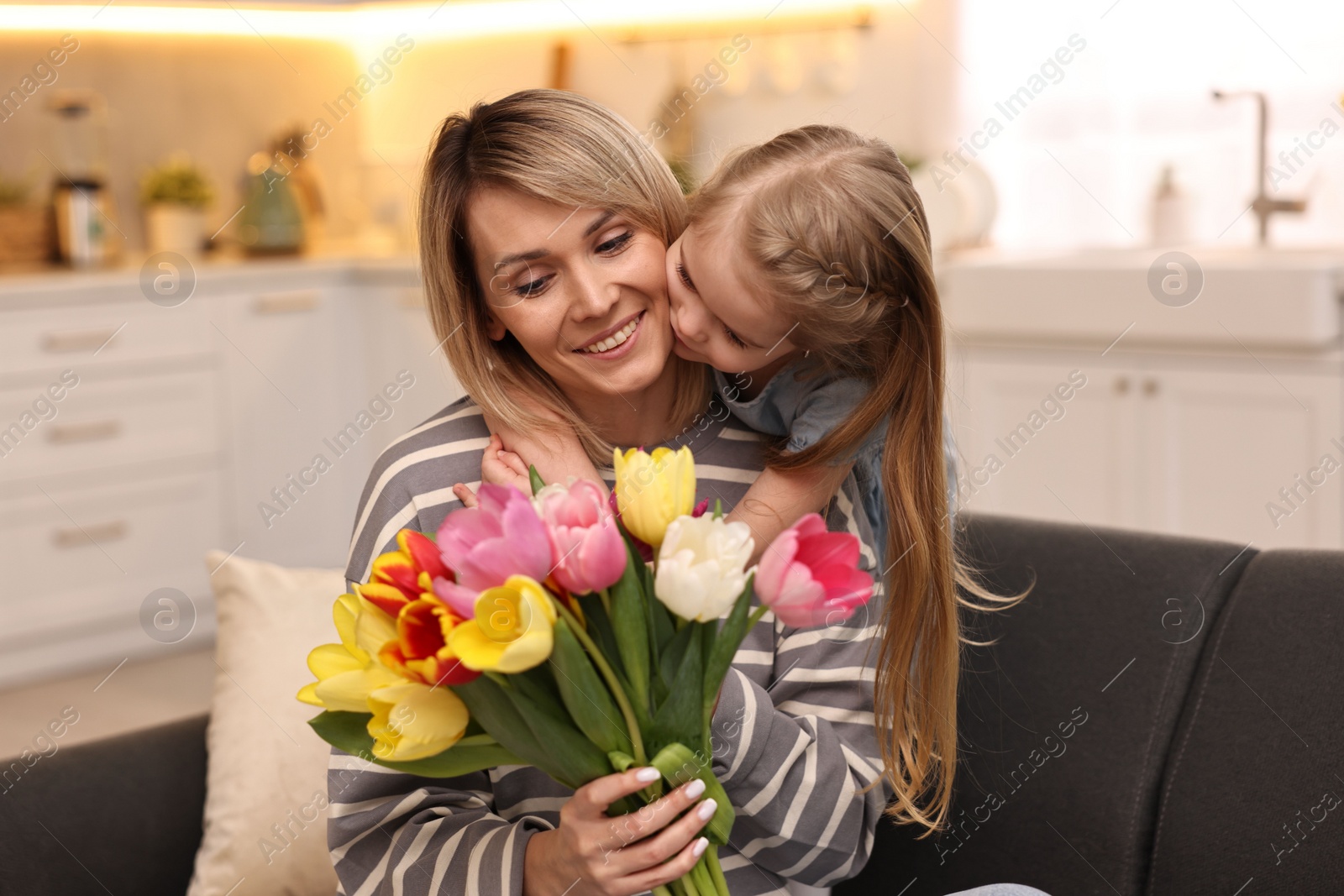 Photo of Little daughter kissing and congratulating her mom with Mother`s Day at home. Woman holding bouquet of beautiful tulips