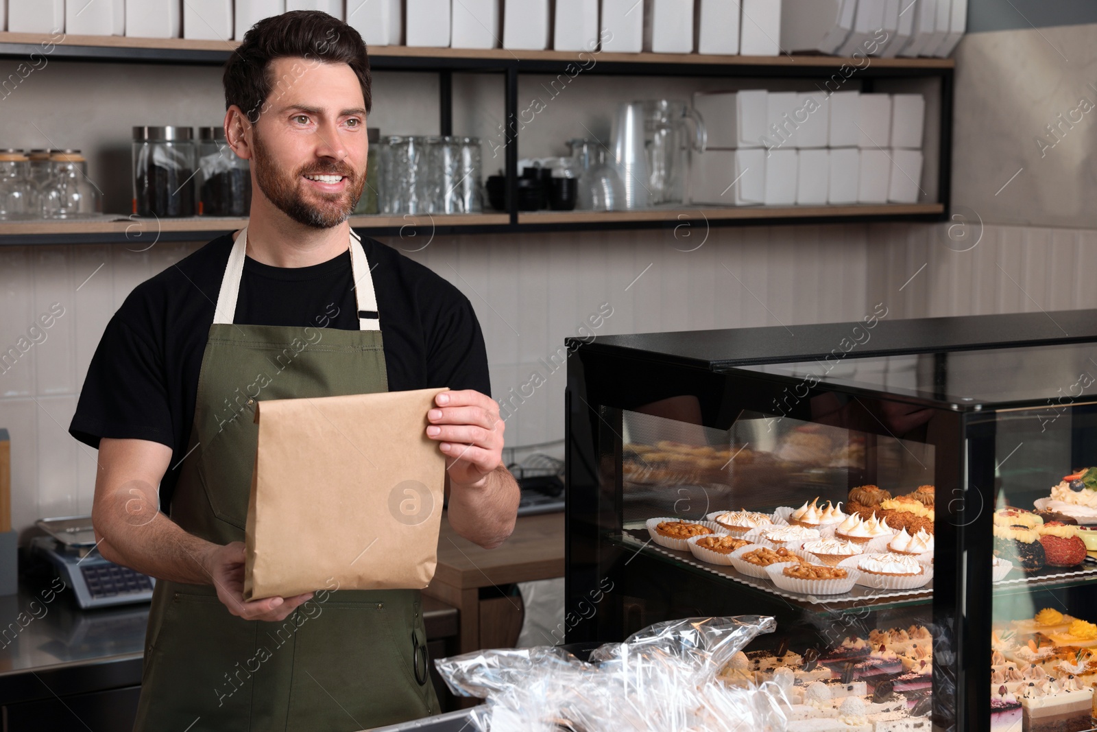 Photo of Happy seller with paper bag at cashier desk in bakery shop