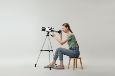 Photo of Young astronomer looking at stars through telescope on grey background