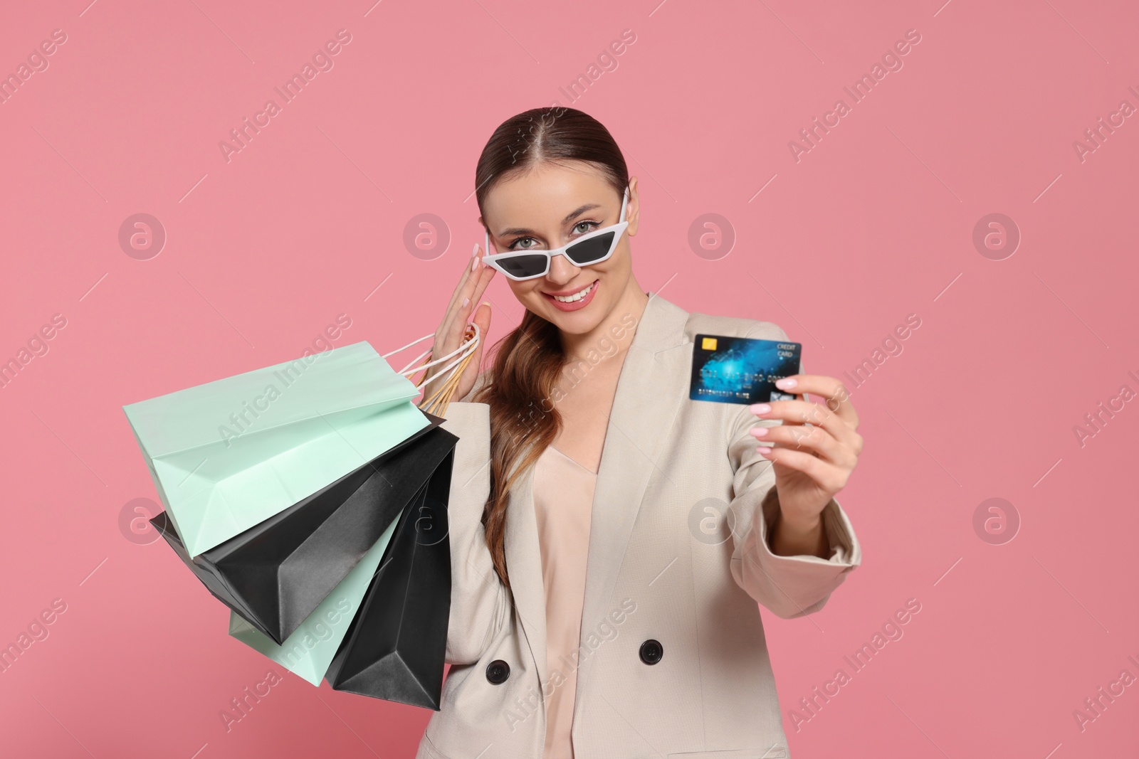 Photo of Stylish young woman with shopping bags and credit card on pink background