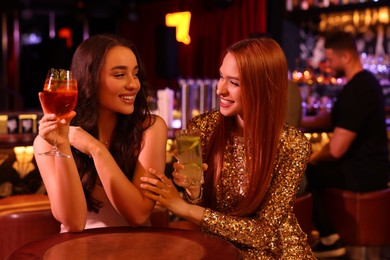 Happy young women with fresh cocktails at table in bar