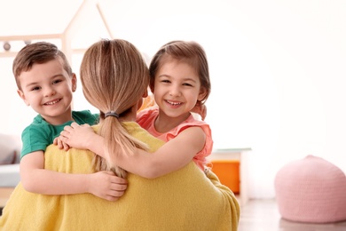 Photo of Cute little children hugging their nanny at home