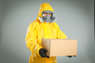 Photo of Man wearing chemical protective suit with cardboard box on light grey background. Prevention of virus spread