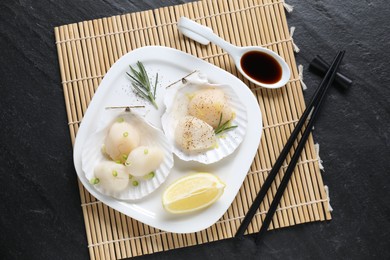 Photo of Raw scallops with green onion, rosemary, lemon and soy sauce on dark textured table, top view