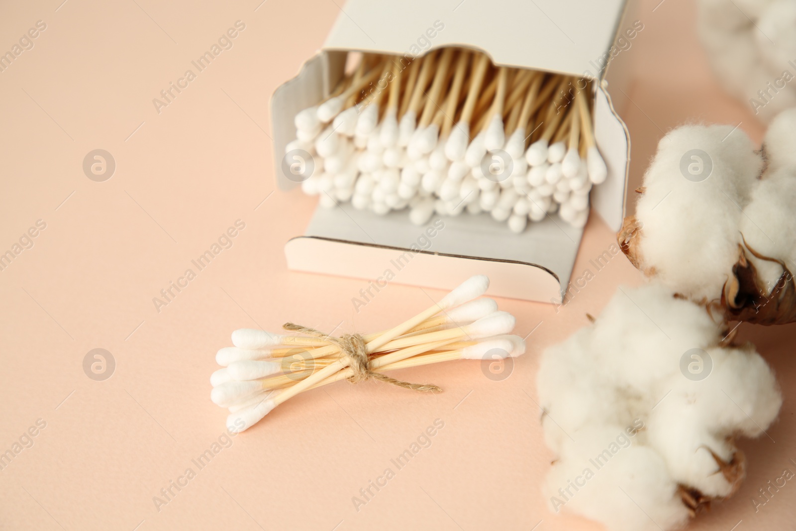 Photo of Cardboard box with cotton buds and flowers on beige background, closeup