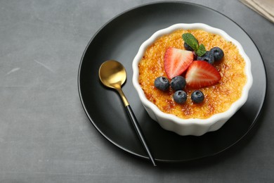 Delicious creme brulee with berries and mint in bowl on grey table, closeup. Space for text