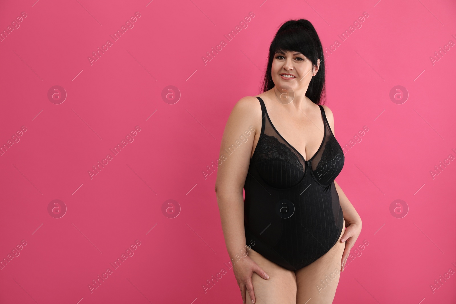 Photo of Beautiful overweight woman in black underwear on pink background, space for text. Plus-size model