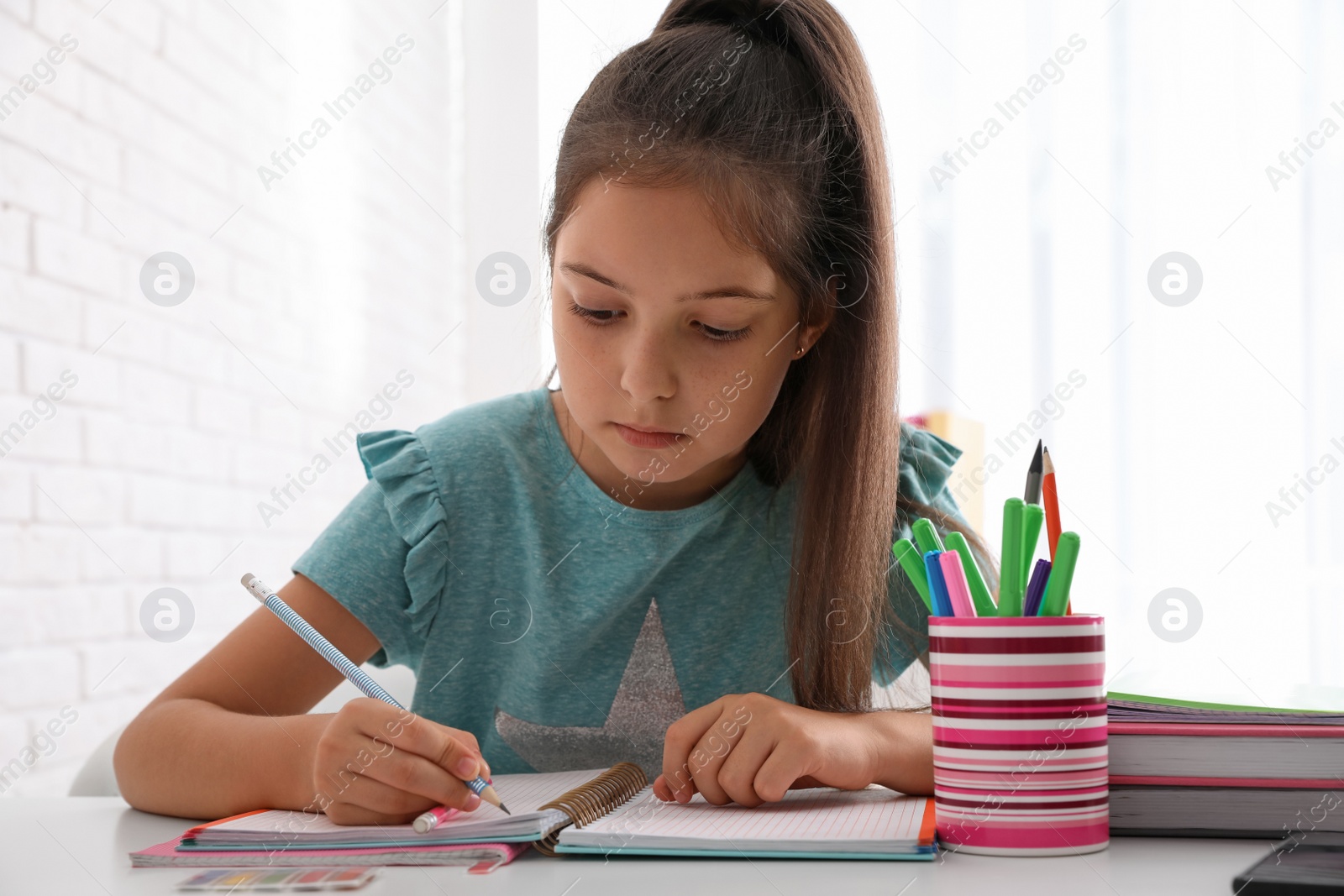 Photo of Pretty preteen girl doing homework at table