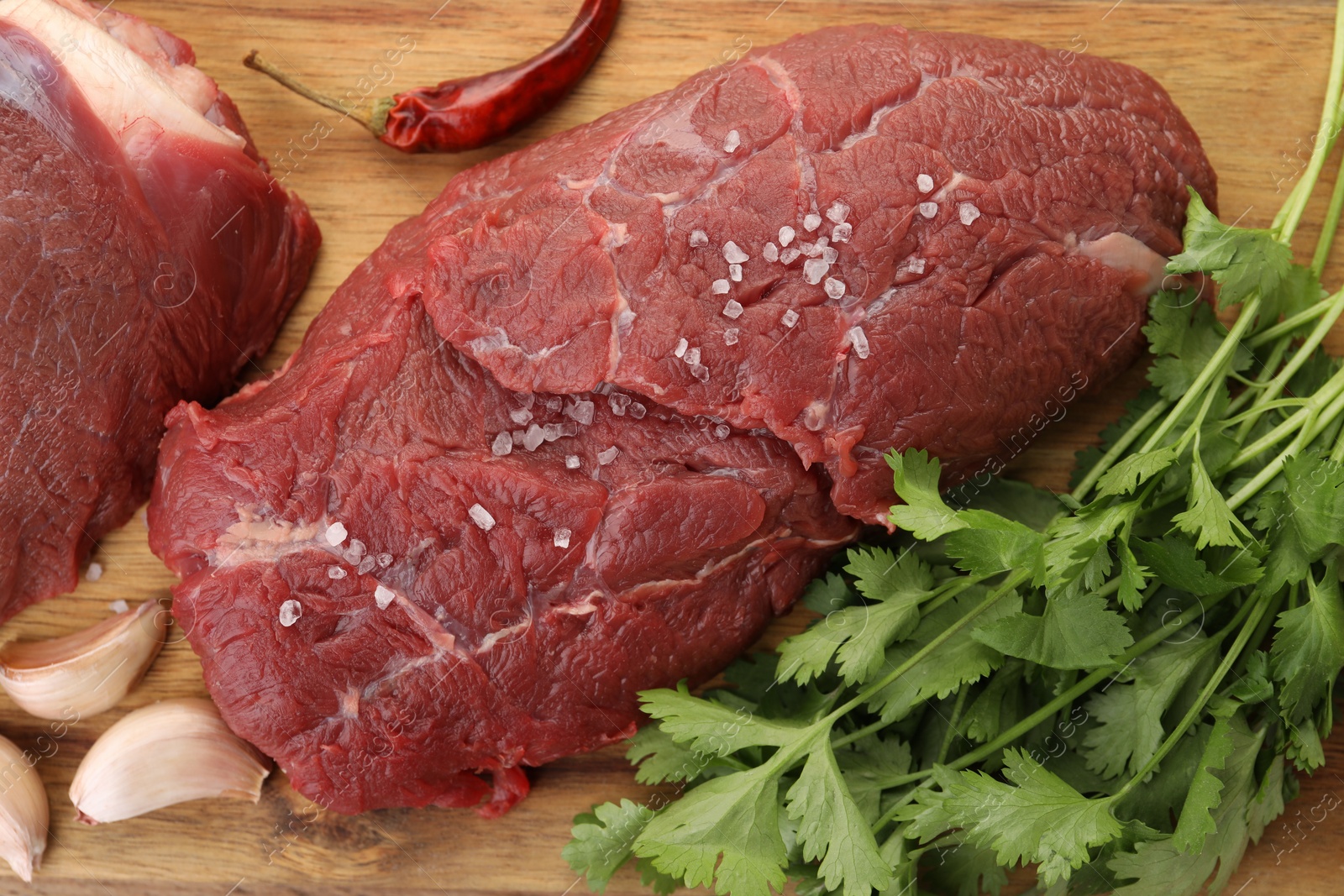 Photo of Pieces of raw beef meat, parsley, garlic and spices on wooden table, flat lay