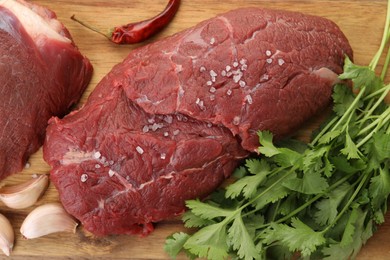 Pieces of raw beef meat, parsley, garlic and spices on wooden table, flat lay