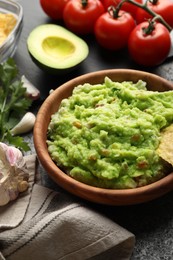 Photo of Delicious guacamole with nachos chips and ingredients on grey table