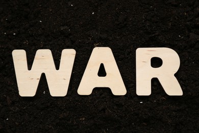 Photo of Word War made of wooden letters on soil, top view