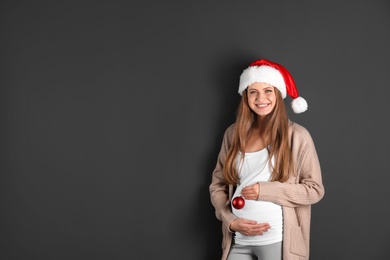 Photo of Young pregnant woman in Santa hat with Christmas decoration on grey background, space for text