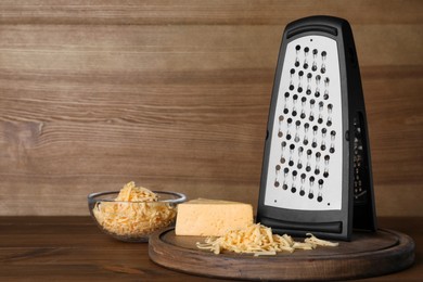 Grater and delicious cheese on wooden table. Space for text