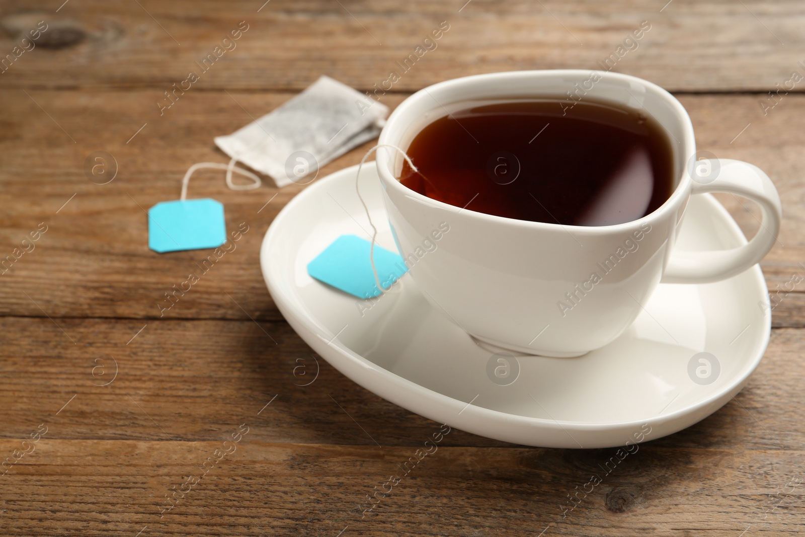 Photo of Tea bag in ceramic cup of hot water on wooden table. Space for text