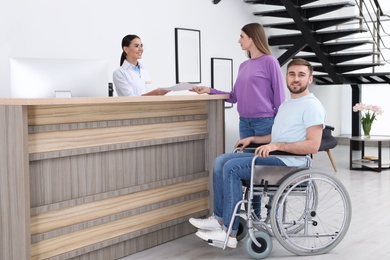 Photo of Woman with man in wheelchair near receptionist at clinic