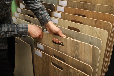 Photo of Man choosing wooden flooring among different samples in shop, closeup