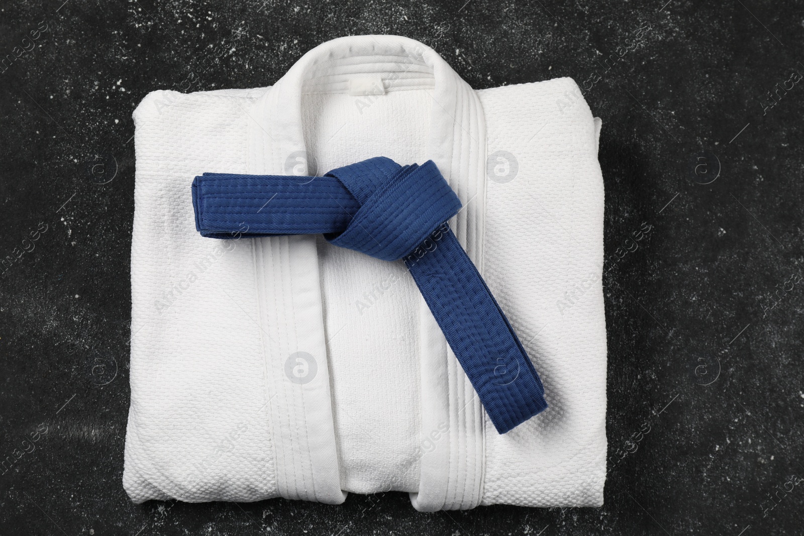 Photo of Blue karate belt and white kimono on gray textured background, top view