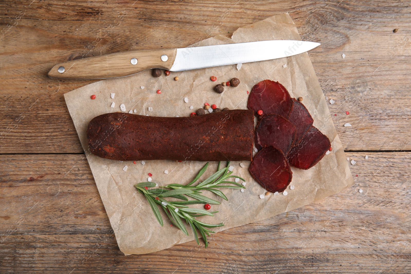 Photo of Delicious dry-cured beef basturma and knife on wooden table, top view