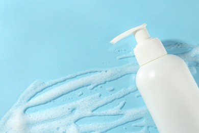 Photo of Bottle with cleansing foam on light blue background, top view and space for text. Cosmetic product