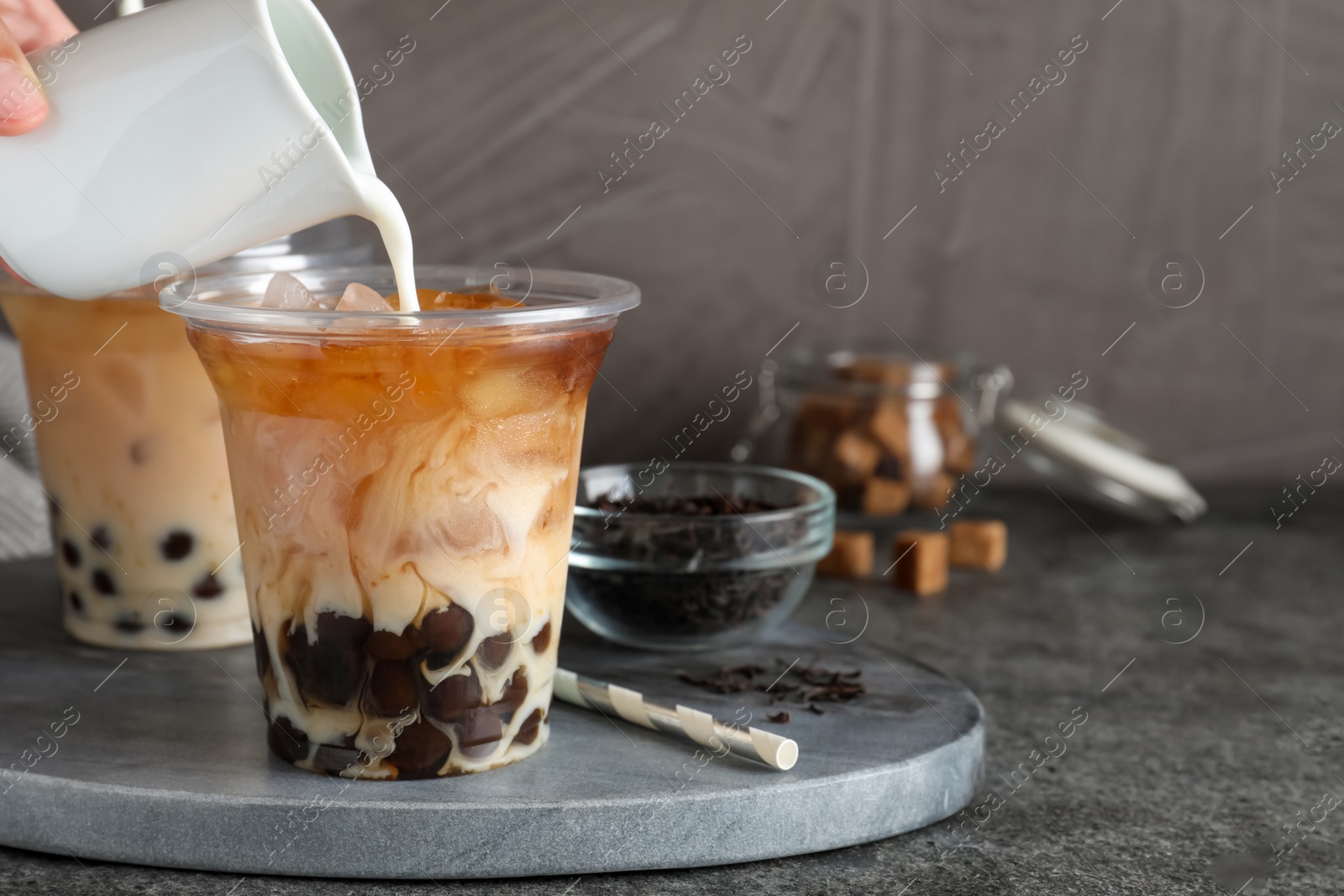 Photo of Person pouring milk into plastic cup with bubble tea at grey table, closeup. Space for text