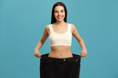 Photo of Happy young woman wearing big jeans after weight loss on turquoise background