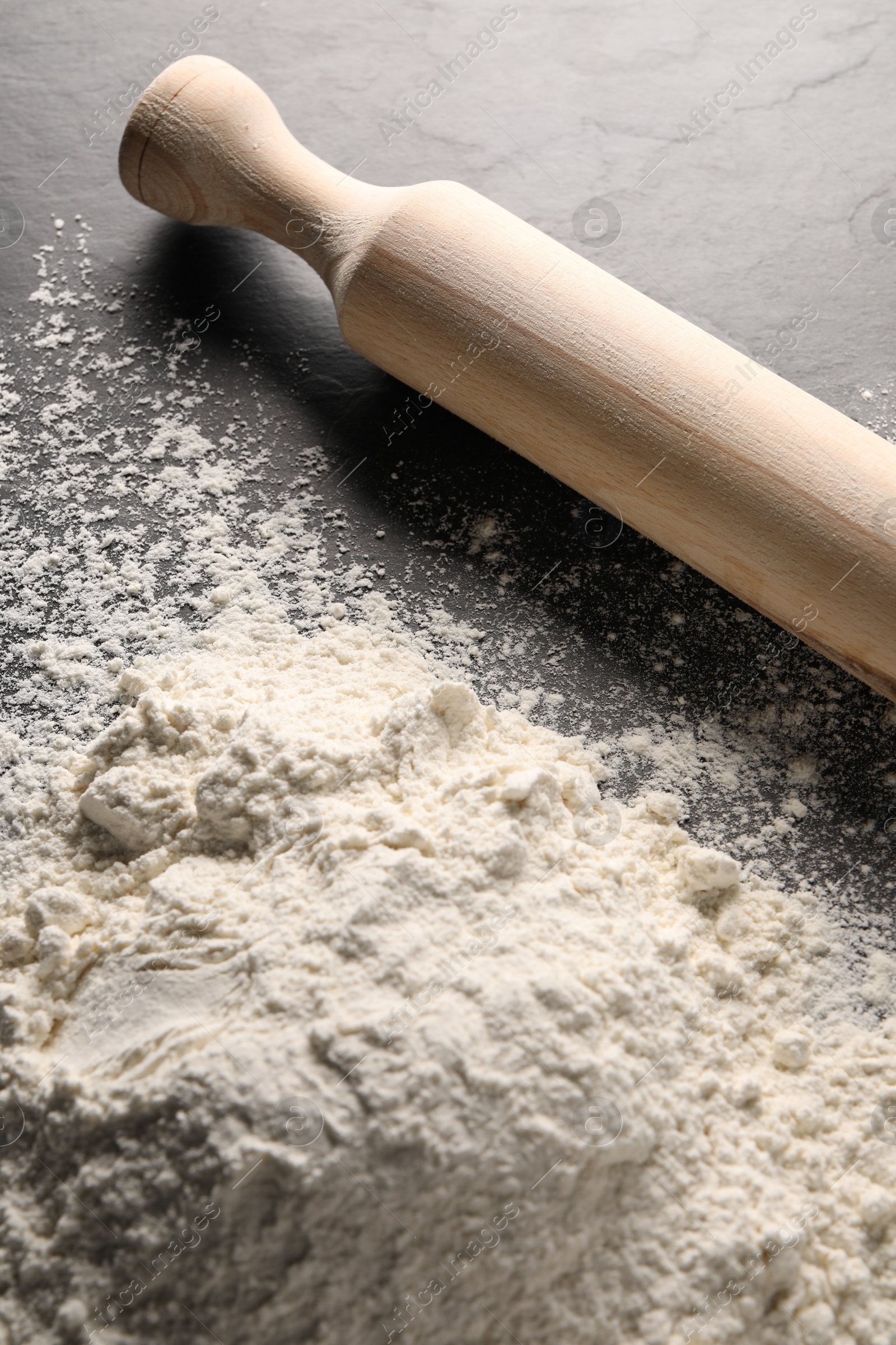 Photo of Pile of flour and rolling pin on grey textured table, closeup