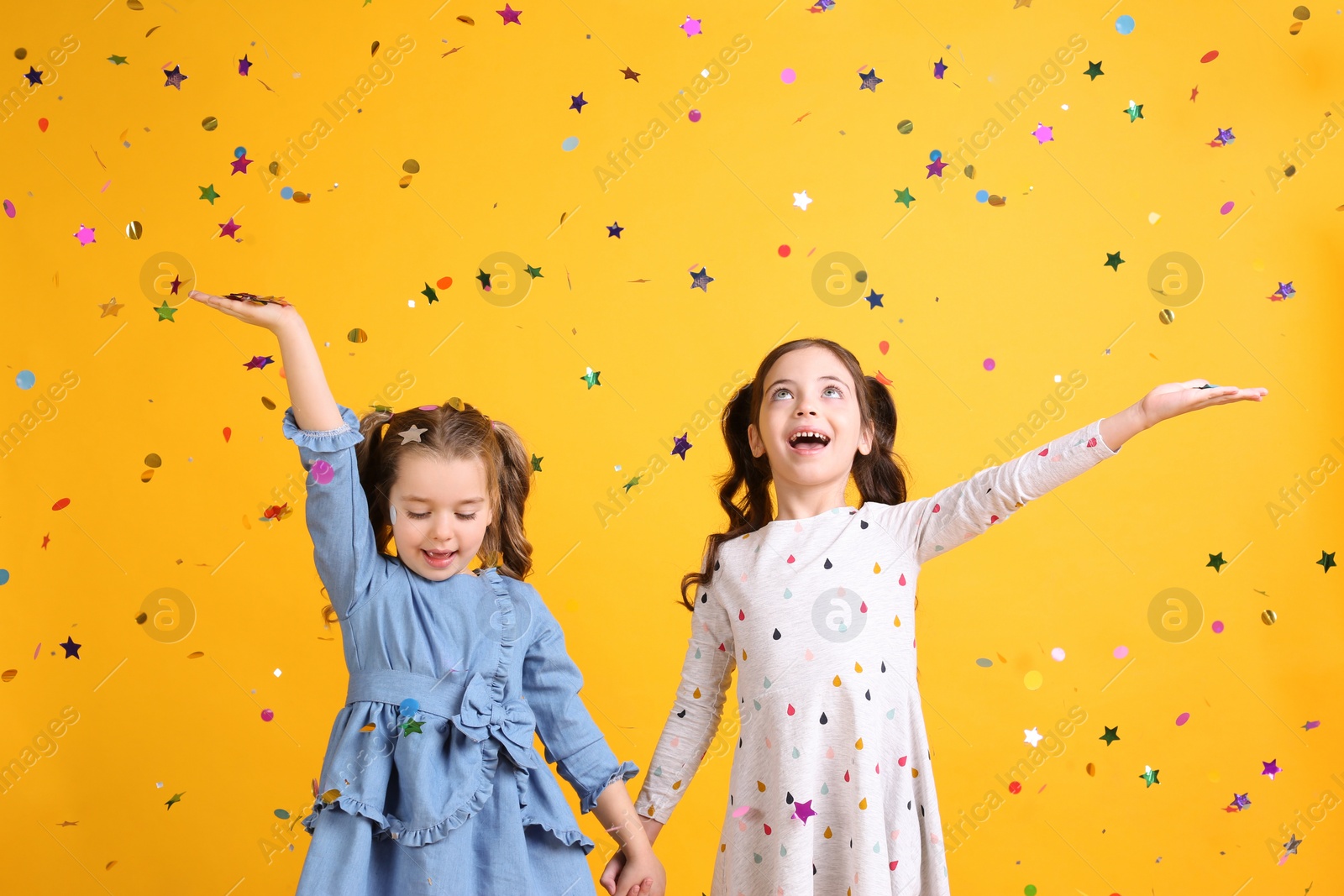 Photo of Adorable little children and falling confetti on yellow background