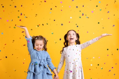 Photo of Adorable little children and falling confetti on yellow background