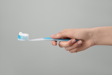 Photo of Woman holding toothbrush with paste on light grey background, closeup