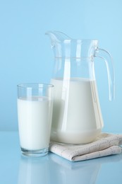 Jug and glass of fresh milk on light blue background