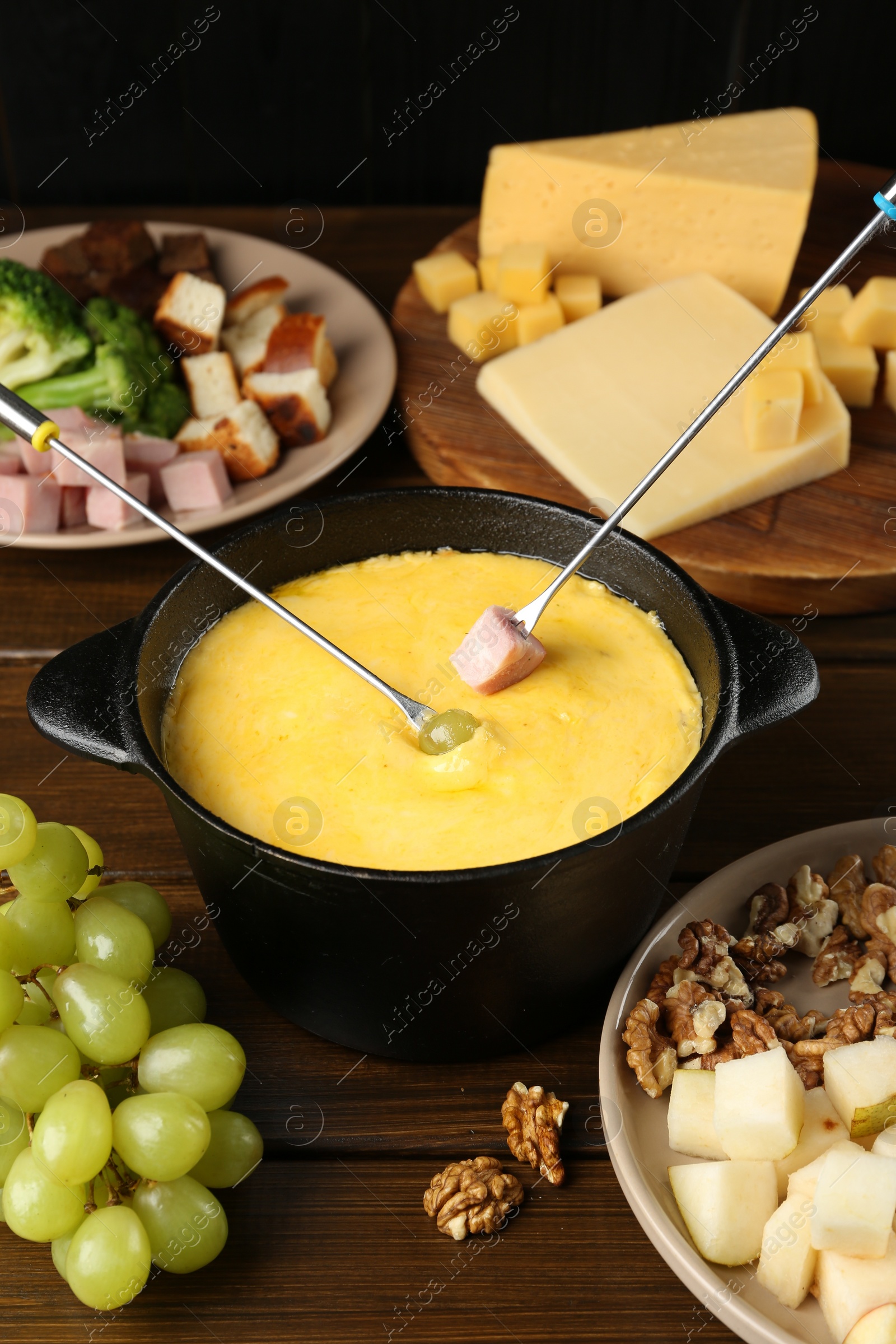 Photo of Fondue pot with melted cheese, forks and different products on wooden table