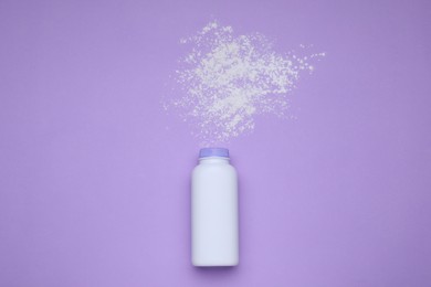 Bottle and scattered dusting powder on violet background, top view. Baby cosmetic product