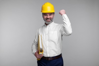 Photo of Architect in hard hat holding folder on grey background
