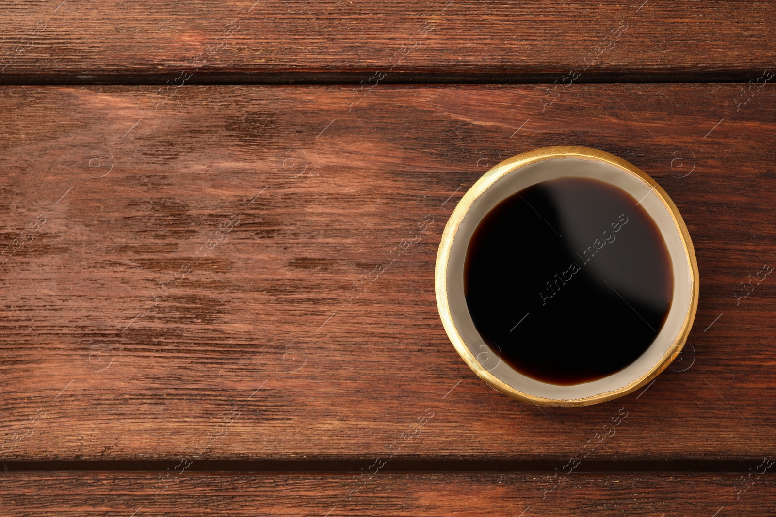 Photo of Bowl with soy sauce on wooden table, top view. Space for text