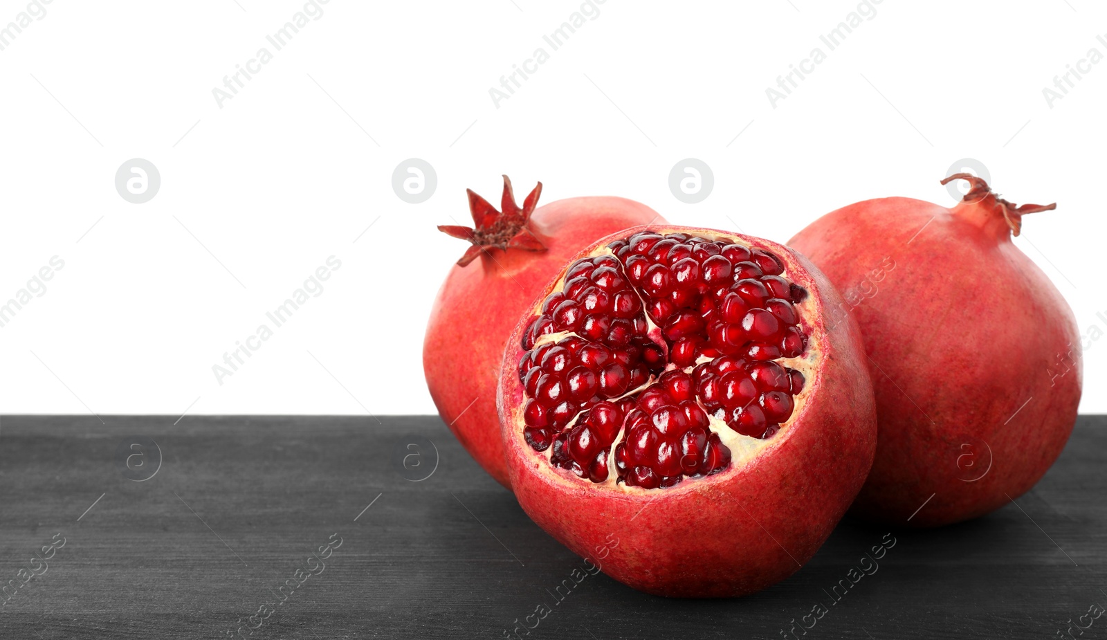 Photo of Fresh pomegranates on black wooden table against white background, space for text