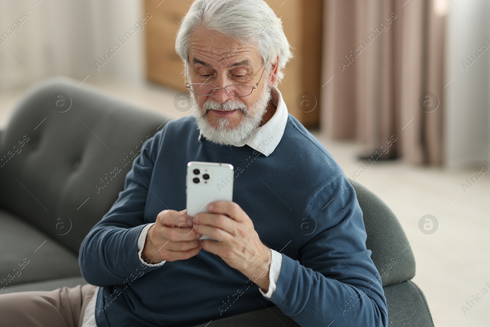 Photo of Portrait of happy grandpa with glasses using smartphone indoors