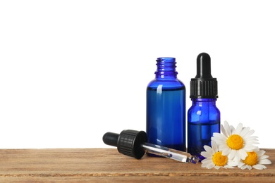 Photo of Chamomile flowers and cosmetic bottles of essential oil on wooden table against white background. Space for text
