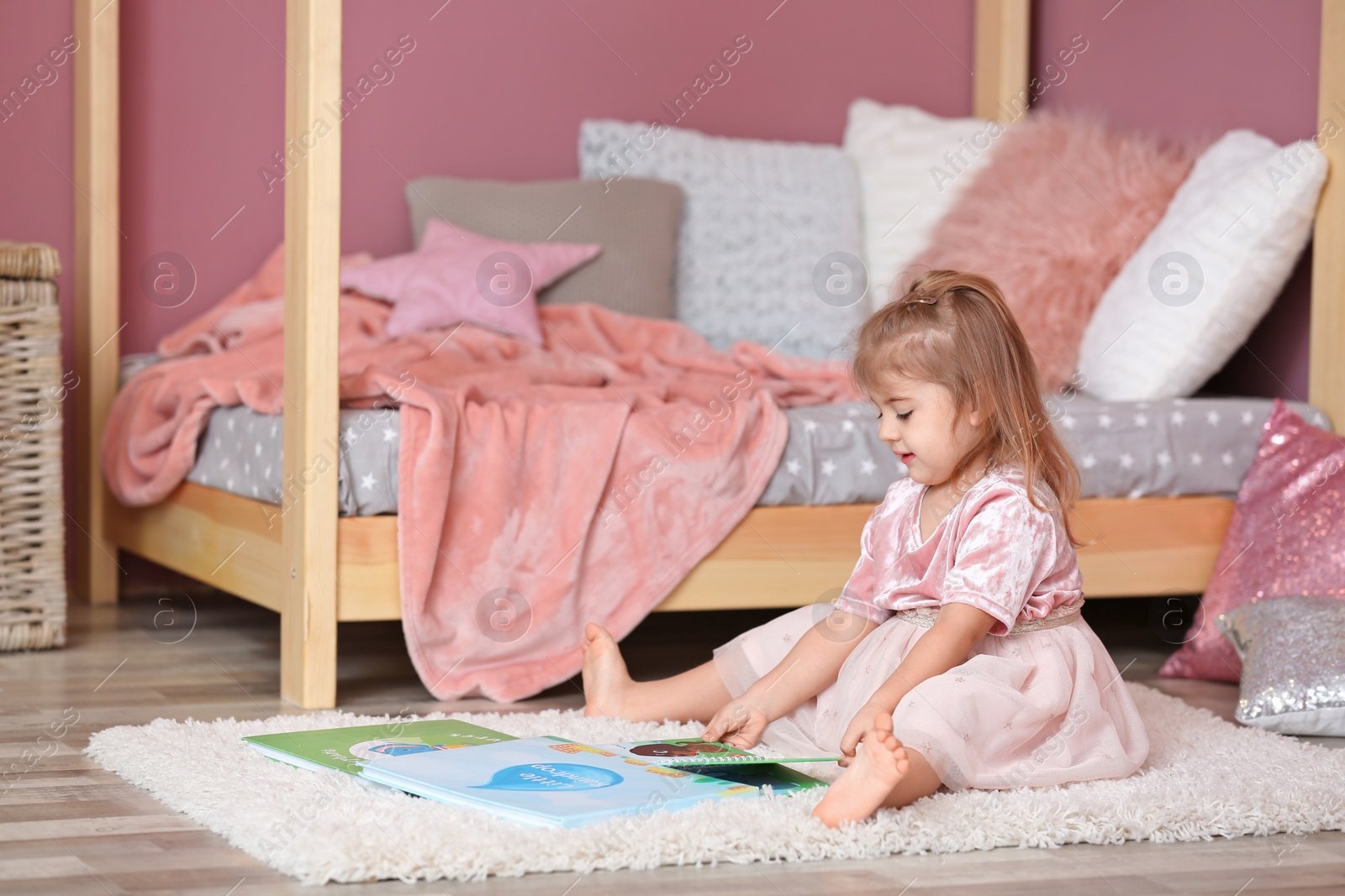 Photo of Cute little girl in princess dress reading book at home