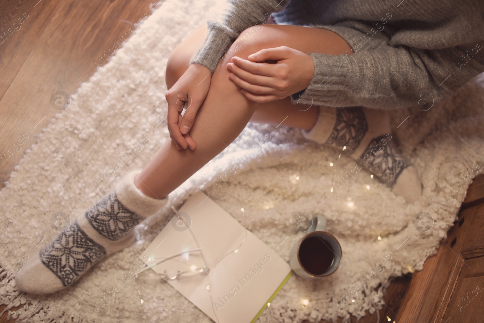 Photo of Woman with cup of hot beverage and book at home in winter evening, top view