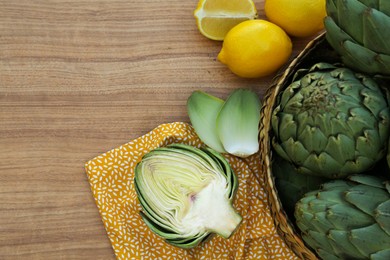 Photo of Artichokes and lemons on wooden table, flat lay