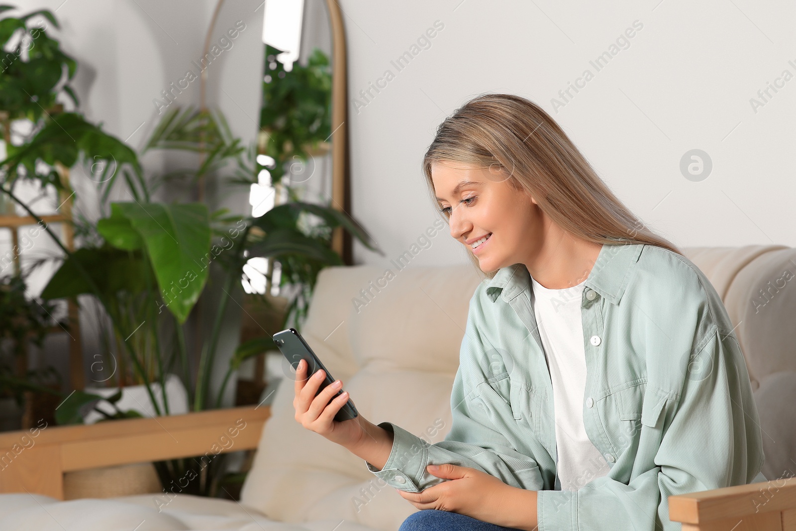 Photo of Woman using smartphone on sofa at home. Space for text