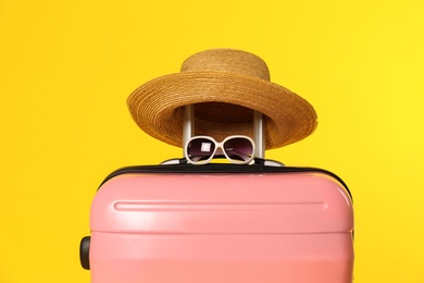 Photo of Stylish suitcase with hat and sunglasses on color background