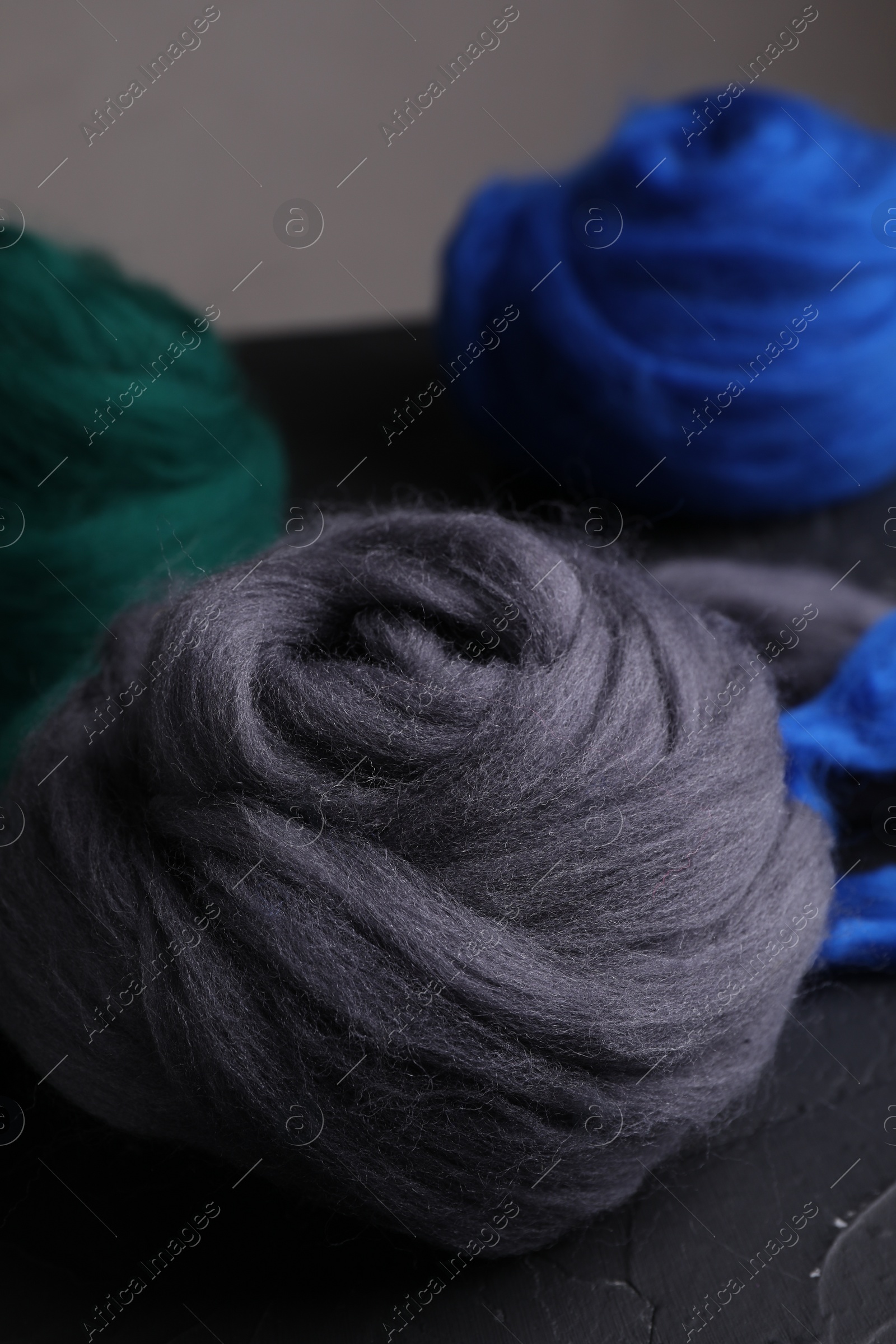 Photo of Colorful felting wool on dark textured table, closeup